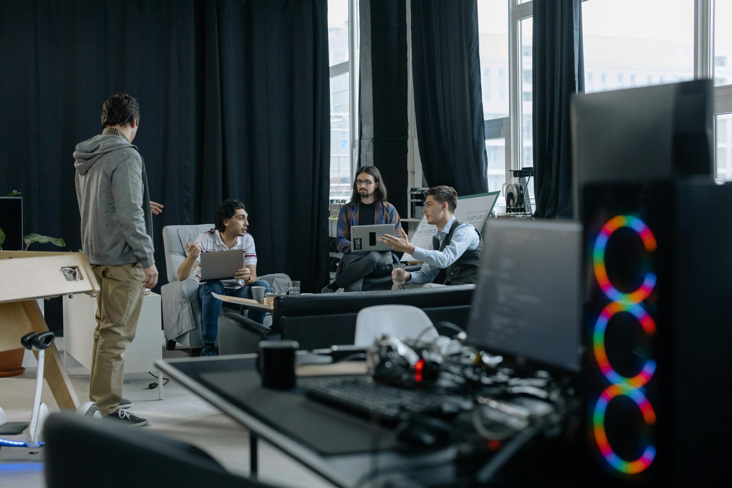 A group of professionals engaged in a casual meeting at a modern office, discussing projects on laptops and tablets.